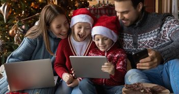 family at Christmas tree with technology