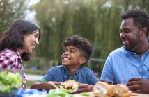 Portrait of multicultural mixed race family with one child enjoying picnic at public park