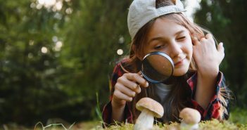 child looking at a mushroom through a magnifying glass